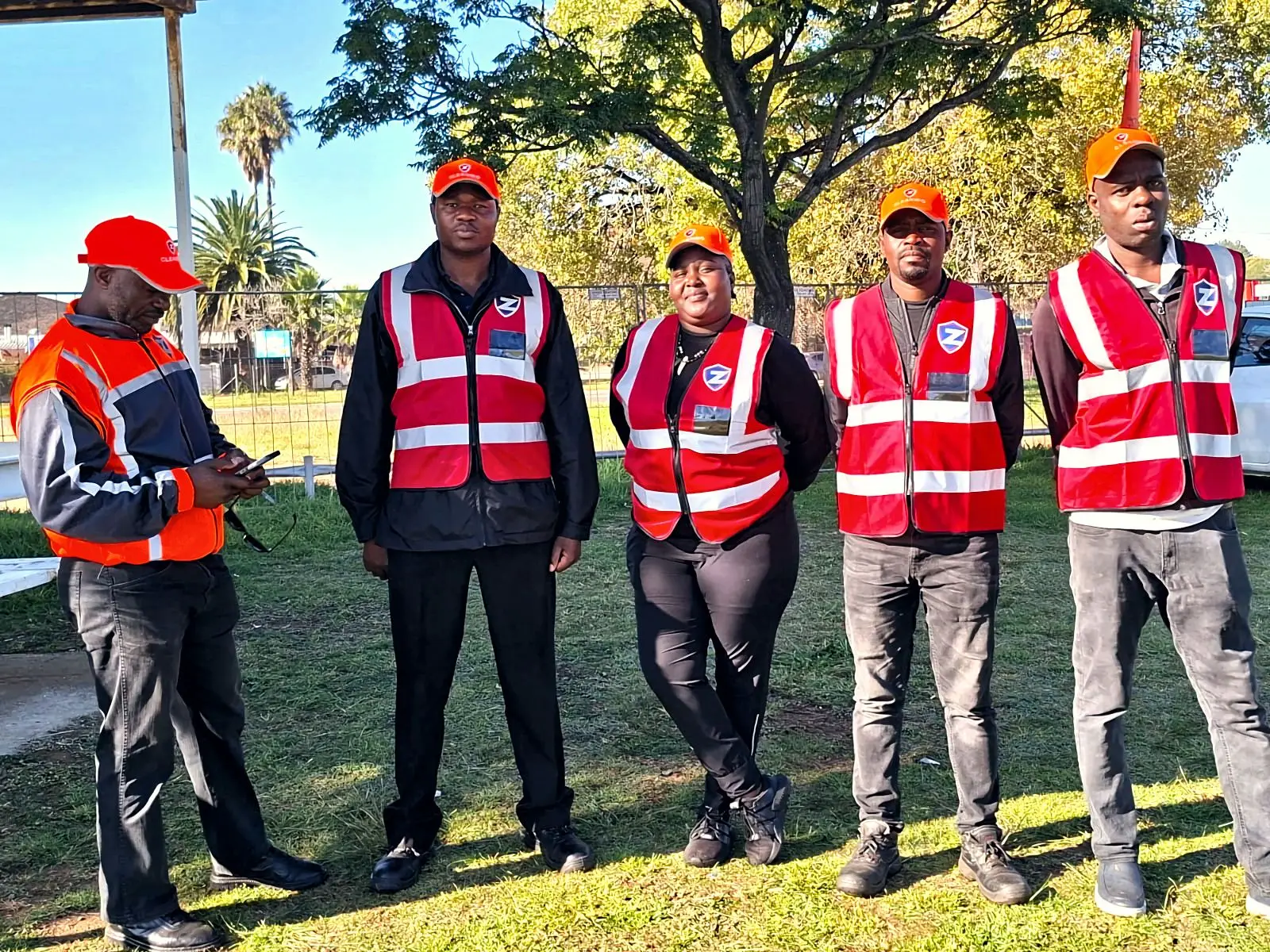 Five ZENOSC event cleaning staff in red vests and orange caps