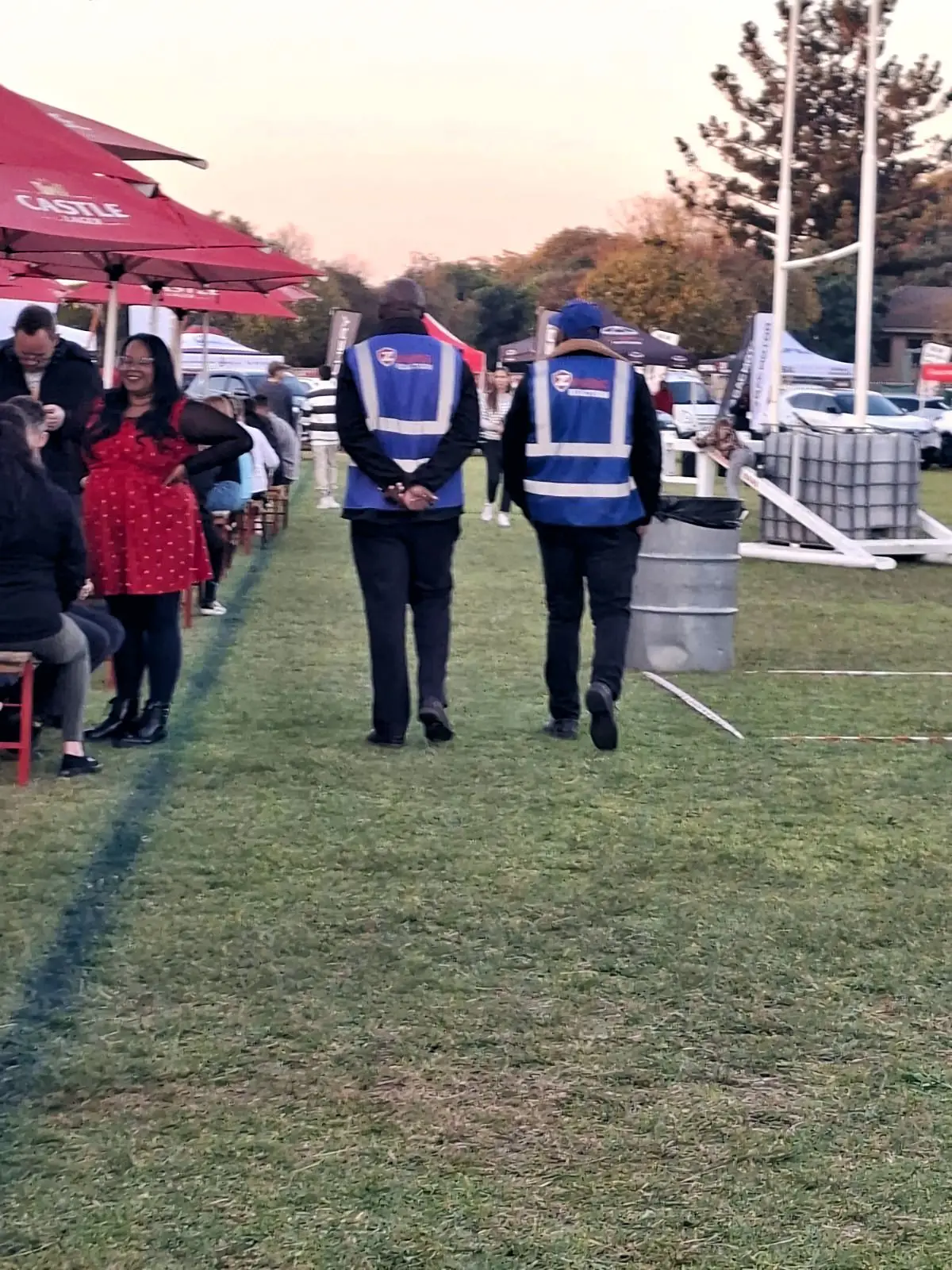 Two ZENOSC officers in royal-blue vests patrolling a festival field at sunset