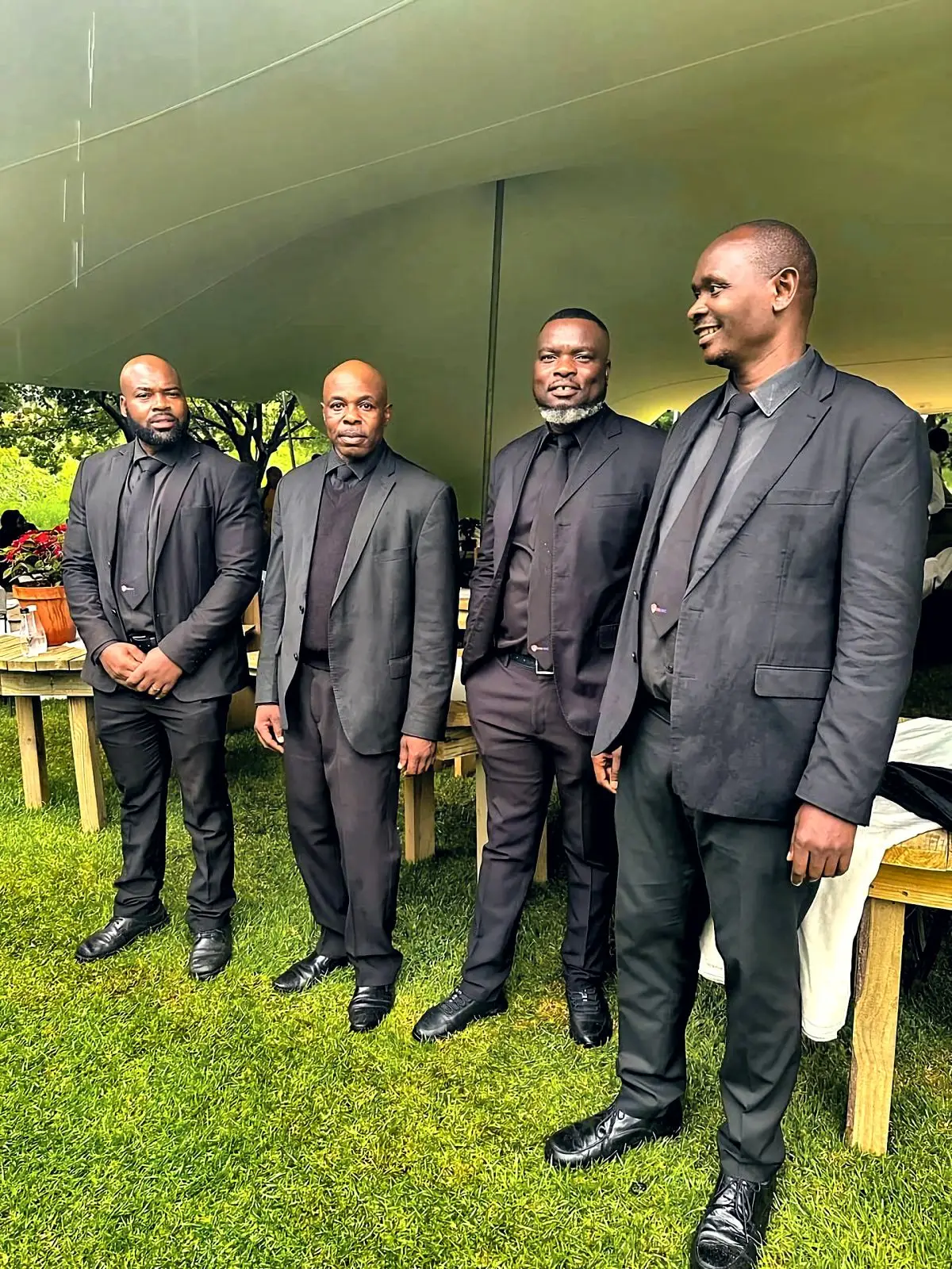 Four ZENOSC protection officers in suits under a garden stretch tent